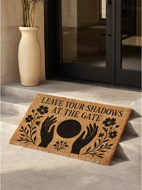 A rectangular, natural brown coir welcome mat with a textured surface, featuring an intricate, black witchy design intended for spiritual protection. The celestial and metaphysical pattern showcases a central manifestation spell circle with sacred geometry, radiating lines, and is accented with stars and crescent moons at the corners, creating a unique piece of entryway decor.